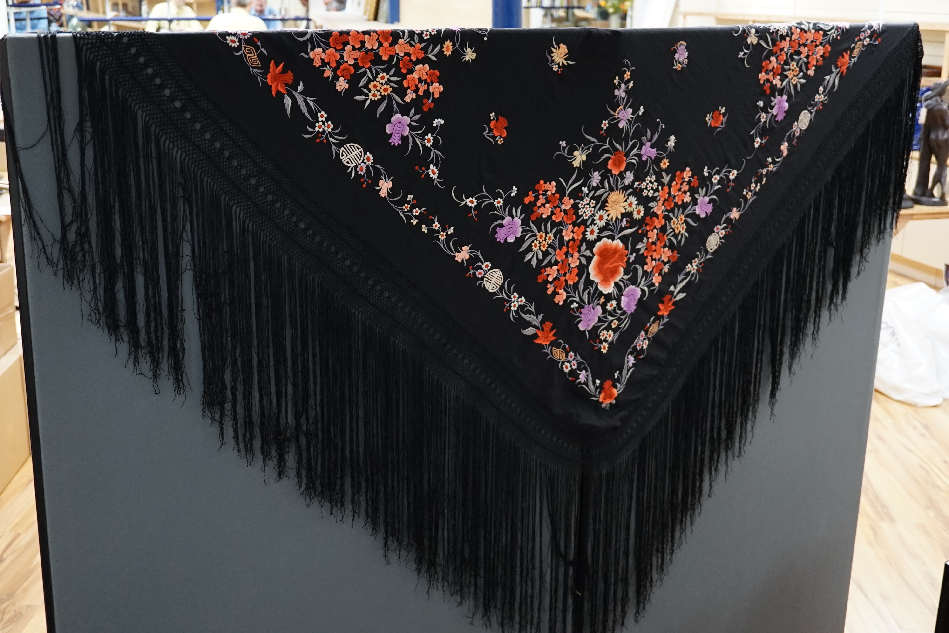 A late 19th / early 20th century Chinese black silk shawl, with polychrome silk embroidered flowers in green, red, orange, lilac, yellow and white, the centre embroidered with, sprigs of multi-coloured flowers, the four